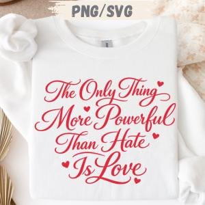 May include: White sweatshirt featuring the red text "The Only Thing More Powerful Than Hate Is Love" in a cursive font. Small red hearts are scattered around the text. The sweatshirt is folded.