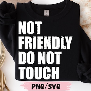May include: Black sweatshirt with the white text "NOT FRIENDLY DO NOT TOUCH". The sweatshirt has a crew neck and long sleeves. The bottom of the image has the text "PNG/SVG" in pink.