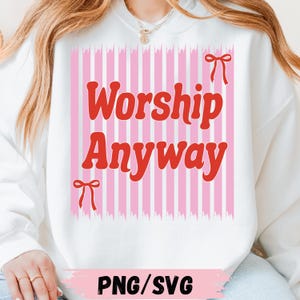 Puede incluir: Sudadera blanca con la frase "Worship Anyway" en rojo sobre un fondo de rayas rosas y blancas, con lazos rojos. La parte inferior de la imagen tiene el texto "PNG/SVG".