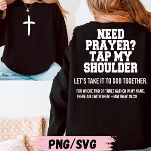May include: Black sweatshirt with the text "NEED PRAYER? TAP MY SHOULDER" in white. Below the text is "LET'S TAKE IT TO GOD TOGETHER." and a Bible verse. A white cross is on the front.