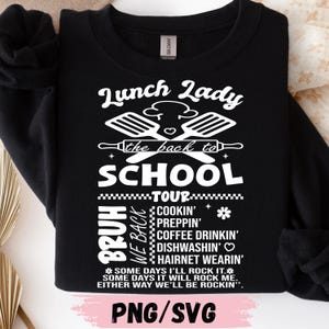 May include: Black sweatshirt with white text that reads "Lunch Lady" above a graphic of cooking utensils and the words "the back to SCHOOL". Below are the words "BRUH WE BACK TOUR COOKIN' PREPPIN' COFFEE DRINKIN' DISHWASHIN' HAIRNET WEARIN'".
