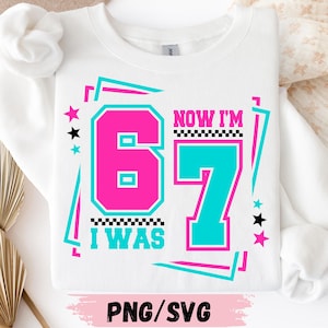May include: White sweatshirt with a retro design. The design features the text "I WAS 67 NOW I'M 67" in pink and teal, with star and line accents. The bottom of the sweatshirt has the text "PNG/SVG".