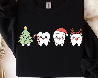 Puede incluir: Una sudadera negra con un estampado gráfico de cuatro personajes de dientes de dibujos animados. Uno es un árbol de Navidad, uno sostiene un bastón de caramelo, uno lleva un gorro y barba de Santa Claus, y uno lleva astas de reno. Texto PNG/SVG visible.