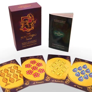 Op de afbeelding: Een paarse doos met gouden letters die "The Macondo Tarot" lezen, ge&iuml;nspireerd door de personages van Gabriel Garcia Marquez. De doos bevat een deck tarotkaarten met illustraties van vissen, bloemen, vlinders en tranen.
