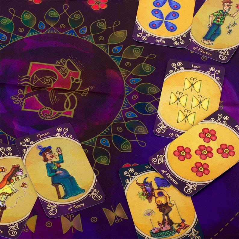 Op de afbeelding: Een tarotkaartendek met een paarse achtergrond en gouden accenten. De kaarten bevatten kleurrijke illustraties van vlinders, bloemen en mensen. De kaarten zijn in een cirkel gerangschikt rond een centrale kaart met een paarse achtergrond en gouden accenten. De centrale kaart bevat een gestileerde afbeelding van een vogel.