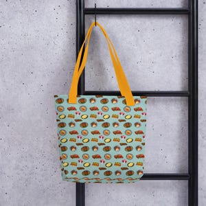 Pu&ograve; includere: Una borsa tote blu con manici gialli presenta un motivo ripetitivo di piatti di cibo colorati. Il cibo include vari piatti come pasta, riso e carne.