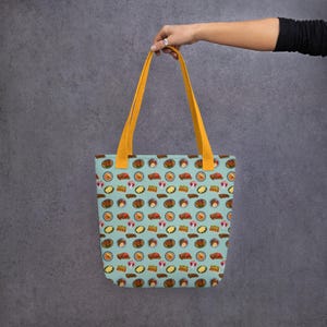 Pu&ograve; includere: Una borsa tote blu chiaro con manici gialli e un motivo di illustrazioni di cibo colorate. La borsa &egrave; realizzata in tela e ha un interno spazioso.