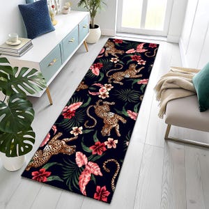 Puede incluir: Una alfombra larga y rectangular con un fondo azul oscuro que presenta un patrón repetido de leopardos, flores tropicales y follaje en tonos de rojo, rosa y verde. Adecuada para un pasillo o entrada.
