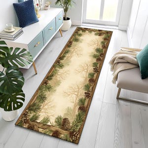 May include: A rectangular area rug with a nature-inspired design. The rug features a central beige field with a forest scene and a border of pine needles and pine cones in shades of green and brown. The rug is placed on a light-colored wooden floor.