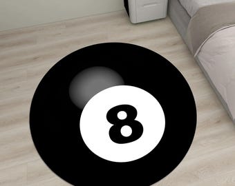 May include: A round black rug featuring a white eight ball design. The number 8 is prominently displayed in the center of a white circle, set against a black background. A gray sphere is visible in the upper portion of the rug.