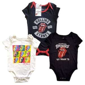 May include: Three baby onesies featuring The Rolling Stones logo. One onesie is white with a colorful graphic of the band's iconic tongue logo. Another onesie is black with a white graphic of the band's name and tongue logo. The third onesie is black with a white graphic of the band's name and tongue logo, and the text "US Tour '78".