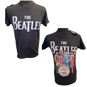 May include: Two black t-shirts featuring "THE BEATLES" in white lettering. One shirt displays the band's name, the other features the band members in colourful outfits with the "Sgt. Pepper's Lonely Hearts Club Band" album artwork.