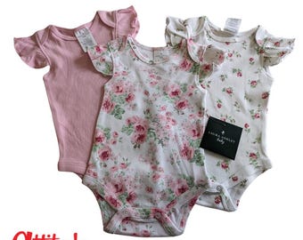 May include: Three baby bodysuits with flutter sleeves. One is solid light pink, while the other two feature a white base with a pink and green floral rose pattern. A black Laura Ashley tag is attached to one of the floral bodysuits.