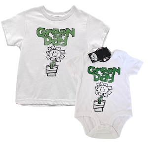 Könnte beinhalten: Weißes T-Shirt und Strampler mit einem grün-weißen Motiv einer Blume mit einem Smiley und dem Text "Green Day".