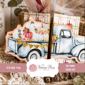 May include: A 3D card folio kit featuring a light blue vintage pickup truck carrying white and pink pumpkins with floral accents. The background displays a green and white plaid pattern with roses. Text reads: IT'S FALL Y'ALL Vintage Press Studio.