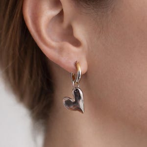 Mixed metal earrings with chrome heart pendant and stainless steel huggie hoops. Two tone gold and silver heart hoop earrings, minimalist lightweight jewelry for everyday wear. Small stainless steel hoops with polished heart charm, hypoallergenic and tarnish resistant. Modern mixed metal earrings perfect for stacking, casual outfits, and gift for her. Two tone huggie hoop earrings with chrome heart pendant, jewelry organizer, small jewelry box, lymare jewels
