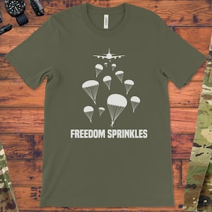 May include: A green t-shirt with a white airplane and parachutes printed on it. The text "FREEDOM SPRINKLES" is printed below the parachutes.