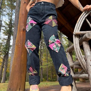 Könnte beinhalten: Schwarze Jeans aus Denim mit mehreren rautenförmigen Patchwork-Einsätzen auf den Vorderbeinen. Die Flicken bestehen aus verschiedenen floralen und geometrischen Stoffmustern in Rosa, Grün, Rot und Schwarz. Die Jeans hat eine hohe Taille.