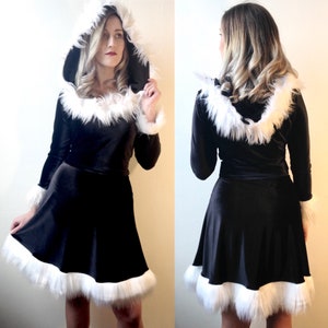 May include: A black velvet dress with long sleeves, a flared skirt, and a hood. The hood, cuffs, and hem are trimmed with fluffy white faux fur. The dress is shown from the front and back, highlighting the design and fit. A festive and elegant garment.