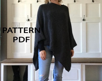 May include: A woman wearing a dark gray poncho with a long, asymmetrical hemline. She is standing in front of a white wall with hooks and shelves. The text "PATTERN PDF" is visible in the lower left corner of the image.