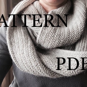 Puede incluir: Una bufanda de punto gris con un patrón de espiga. La bufanda la lleva puesta una persona y el texto "PATTERN PDF" es visible en la bufanda.