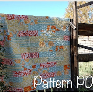 Puede incluir: Una colcha colorida con un diseño de patchwork que presenta motivos florales de color naranja, amarillo, azul y blanco. La colcha está colgada en una valla de madera con el texto "Pattern PDF" escrito debajo.