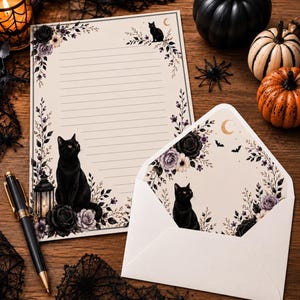 May include: A cream-colored stationery set featuring a lined sheet and an envelope, both decorated with black cats, dark roses, purple flowers, crescent moons, and bats. A black fountain pen with gold accents rests beside the paper.