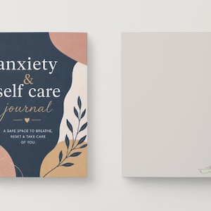 May include: A spiral-bound journal with a navy blue cover featuring the words "anxiety & self care journal" in white and gold script. The cover also includes abstract shapes in peach and beige, and a botanical illustration. The journal is open to a blank page.