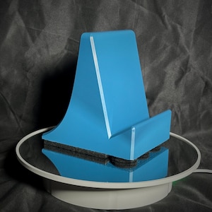 Peut inclure: Un support de téléphone bleu clair avec une bande blanche sur le devant. Le support est posé sur une plateforme circulaire blanche.