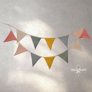 Könnte beinhalten: Eine Girlande mit dreieckigen Flaggen in den Farben Rosa, Gelb, Grau und Grün. Die Flaggen sind mit weißem Garn zusammengenäht und an einer weißen Schnur befestigt.