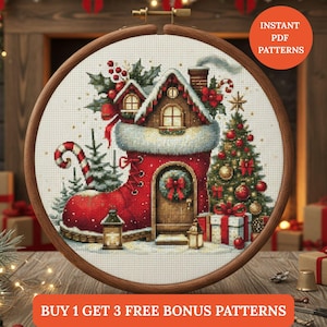 Puede incluir: Un diseño de punto de cruz en un aro de madera representa una escena navideña. Una casa roja en forma de bota con un tejado cubierto de nieve y un árbol de Navidad está rodeada de regalos y faroles. El texto "INSTANT PDF PATTERNS" y "BUY 1 GET 3 FREE BONUS PATTERNS" son visibles.