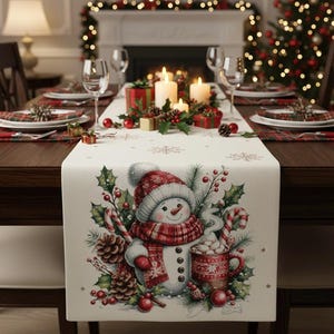 May include: A festive Christmas table setting featuring a snowman-themed table runner. The runner has a snowman illustration with a red and white hat and scarf, surrounded by holly, candy canes, and pine cones. The table is set with plates, glasses, and candles.