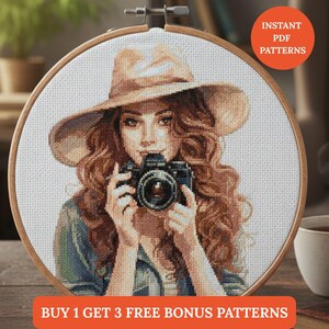Puede incluir: Bordado de punto de cruz de una mujer con sombrero sosteniendo una cámara. La mujer tiene el pelo largo y ondulado de color marrón. El bordado está colocado en un aro de madera. El texto en la imagen dice "Instant PDF Patterns" y "Buy 1 Get 3 Free Bonus Patterns."