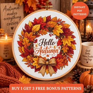 Op de afbeelding: Een ronde borduurring met een kruissteekpatroon van een herfstkrans gemaakt van rode, oranje en gele esdoornbladeren, eikels en bessen. In het midden staat de tekst Hello Autumn in cursief schrift met een beige strik aan de onderkant.