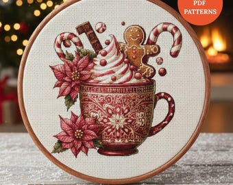 May include: Cross-stitch embroidery in a wooden hoop features a festive holiday design. A red mug is filled with whipped cream, candy canes, and a gingerbread man. The design includes poinsettias and the text "Instant PDF Patterns".