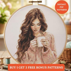 Può includere: Un modello a punto croce di una donna con lunghi capelli castani che tiene in mano una tazza bianca, incorniciato in un telaio da ricamo in legno. La donna indossa un maglione rosa. L'immagine include il testo "Instant PDF Patterns" e "Buy 1 Get 3 Free Bonus Patterns."