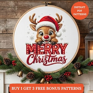 May include: A round wooden embroidery hoop containing a white fabric panel with a cross-stitch design of a brown reindeer wearing a red Santa hat, positioned above the red text MERRY Christmas, surrounded by small white snowflake illustrations.