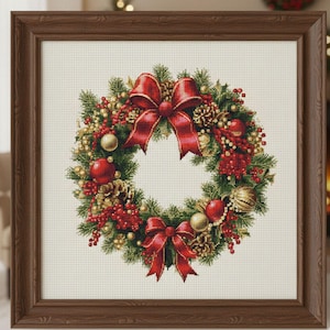 May include: A framed cross-stitch of a Christmas wreath. The wreath features red bows, berries, and ornaments, along with pinecones and greenery. The frame is a dark brown color.