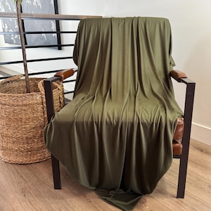 May include: A dark green throw blanket draped over a brown leather armchair with black metal legs.