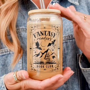 May include: A glass can with a bamboo lid and a straw. The can has a black and white graphic that says "Fantasy Readers Book Club" with a dragon and a ship.