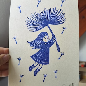 Peut inclure: Une impression couleur crème présentant une illustration à l'encre bleue d'une personne aux cheveux longs portant une robe et des chaussettes, flottant tout en tenant une grande aigrette de pissenlit. Des graines flottent autour.