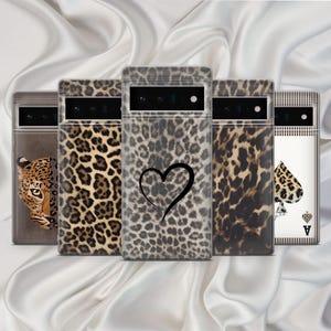 May include: A selection of phone cases with diverse patterns. The cases showcase a leopard print, a leopard's face, a black heart, and an ace of spades card design. The cases are transparent with printed designs, set against a white satin backdrop.