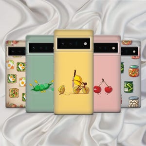 May include: Five different phone cases with various designs. The cases are all yellow, green, pink, and white with different food illustrations. The designs include a lemon on a bicycle, a cherry, a pickle, a lemon slice, and a green leafy vegetable.