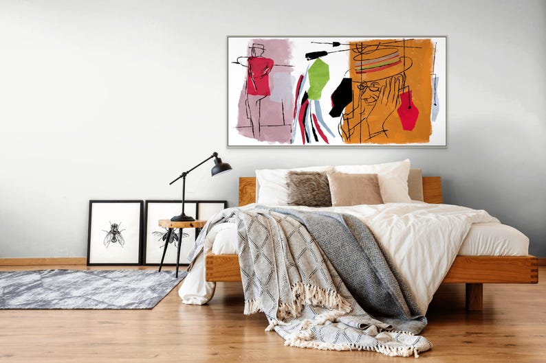 K&ouml;nnte beinhalten: Ein Schlafzimmer-Interieur mit einem wei&szlig;en Bett, einem h&ouml;lzernen Kopfteil und einer wei&szlig;en Decke. Ein gerahmtes abstraktes Gem&auml;lde mit einer Person in einem roten Hemd und einer Person mit Hut und Brille h&auml;ngt &uuml;ber dem Bett. An der Wand links vom Bett befinden sich zwei schwarze gerahmte Drucke.