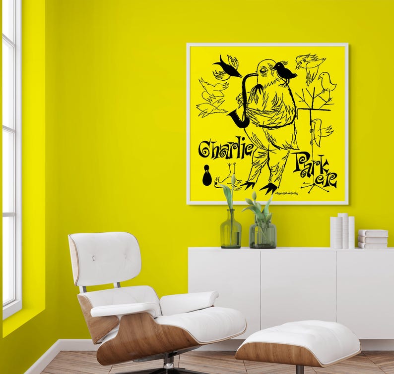 May include: A black and white illustration of a bird playing a saxophone with the text "Charlie Parker" on a yellow background. The illustration is framed and hanging on a yellow wall.