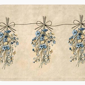 May include: A rectangular bath mat featuring three bunches of blue and cream-colored flowers hanging from a string. Each bunch is tied with a dark brown bow. The background is a light beige color.