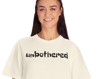 May include: A white t-shirt with the word "unbothered" printed in black on the front.