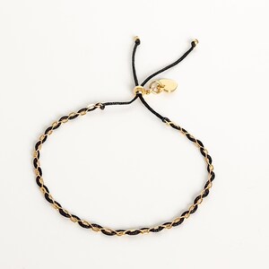 May include: An adjustable bracelet with a heart charm. The bracelet is made of a braided cord and a gold chain.