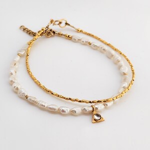 May include: A delicate gold chain bracelet with a small triangle charm and a strand of white pearls.
