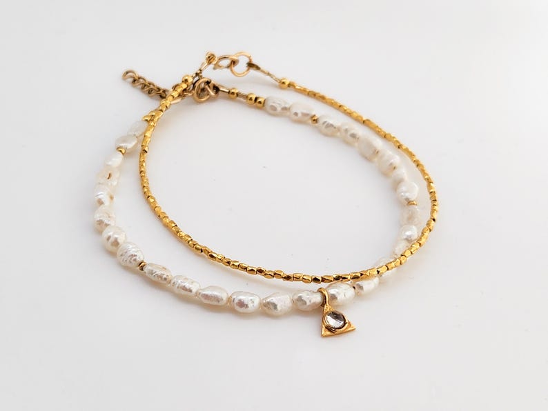 May include: A delicate gold chain bracelet with a small triangle charm and a strand of white pearls.